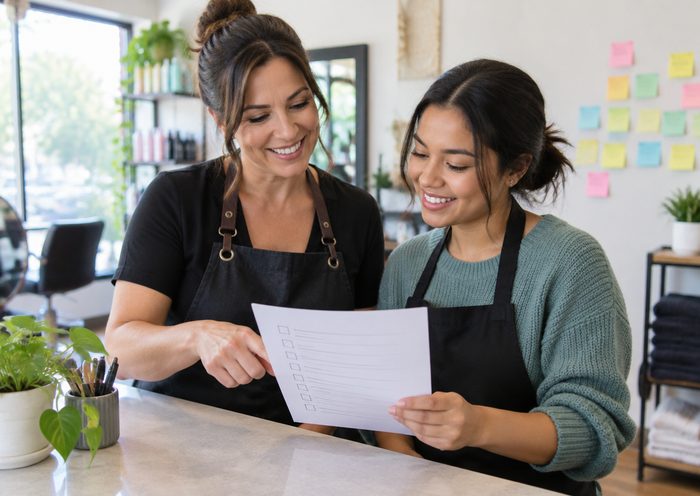 A salon owner and her assistant smiling over a one-page checklist at the front counter